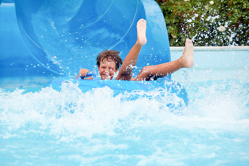 feliz un niño de 8 años está montando en el parque acuático en círculos inflables en toboganes de agua con salpicaduras photo