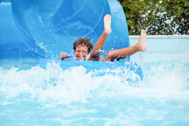 happy an 8 year old boy is riding in the water Park on inflatable circles on water slides with splash stock photo