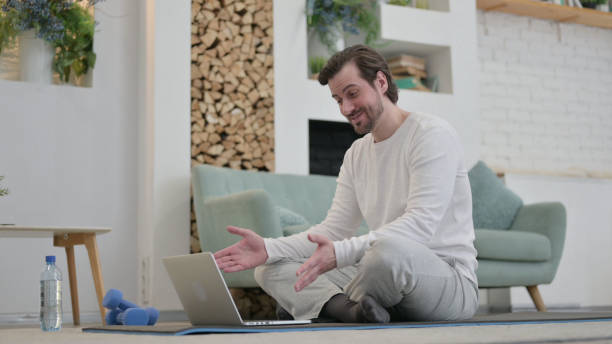 giovane uomo che parla in videochiamata sul tappetino per l'esercizio del computer portatile a casa - 24200 foto e immagini stock