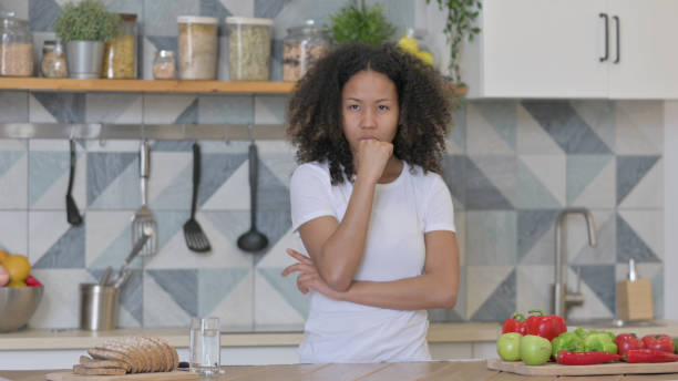 istock Young African Woman Thinking while Standing in Kitchen 1345619380