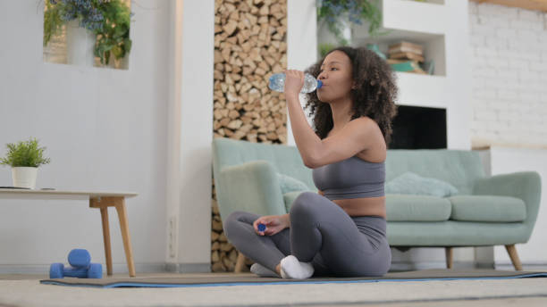 istock Tired African Woman Drinking Water while doing Yoga at Home 1345619556