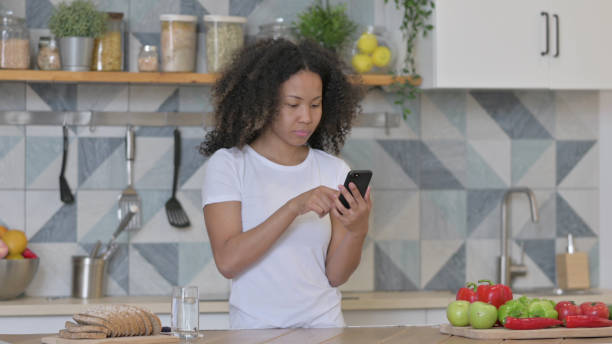 istock Young African Woman using Smartphone in Kitchen 1345619561