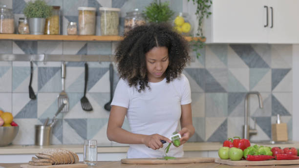 istock Attractive Young African Woman Peeling Cucumber in Kitchen 1345620213