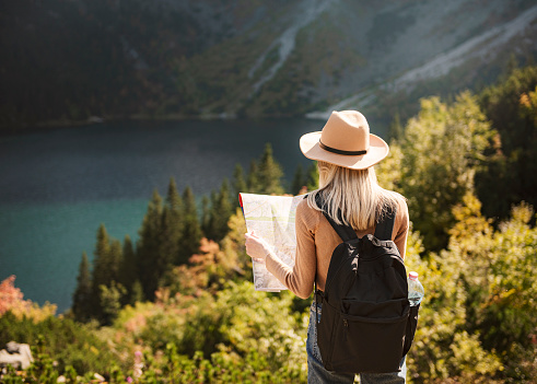 Woman traveler wearing hat and looking at amazing mountains and lake, wanderlust travel concept. Lake Morskoy Eye in the Polish Tatras.