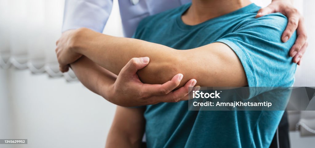 Man physiotherapist stretching shoulder and arm patient at a clinic. Human Spine Stock Photo