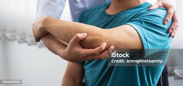 Man Physiotherapist Stretching Shoulder And Arm Patient At A Clinic Stock Photo - Download Image Now