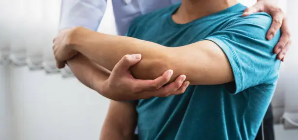 Photo of Man physiotherapist stretching shoulder and arm patient at a clinic.