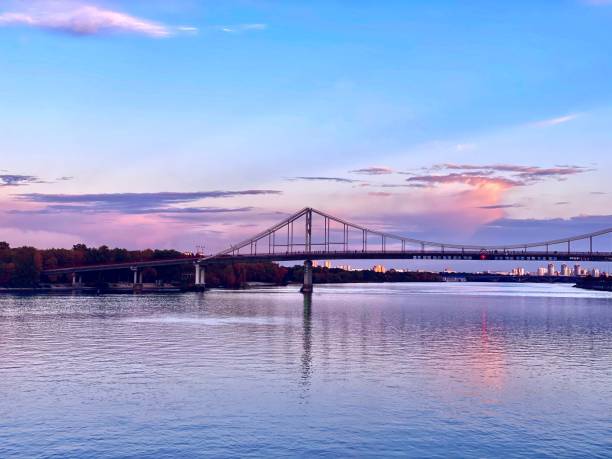 istock Beautiful sunset over river. Pedestrian crossing bridge across Dnieper river against the background of evening sunset. Beautiful views of Kiev city at night. Scenic evening dusk cityscape. 1345632507