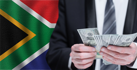 Hands holding dollar money on flag of South Africa