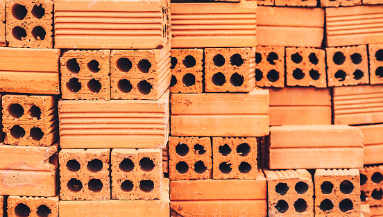 Close up pile new red brick with holes stacked in rows wall. Store of bricks ready for building or sale. Background Building Construction materials Texture, outdoor storage or manufacturing concept.