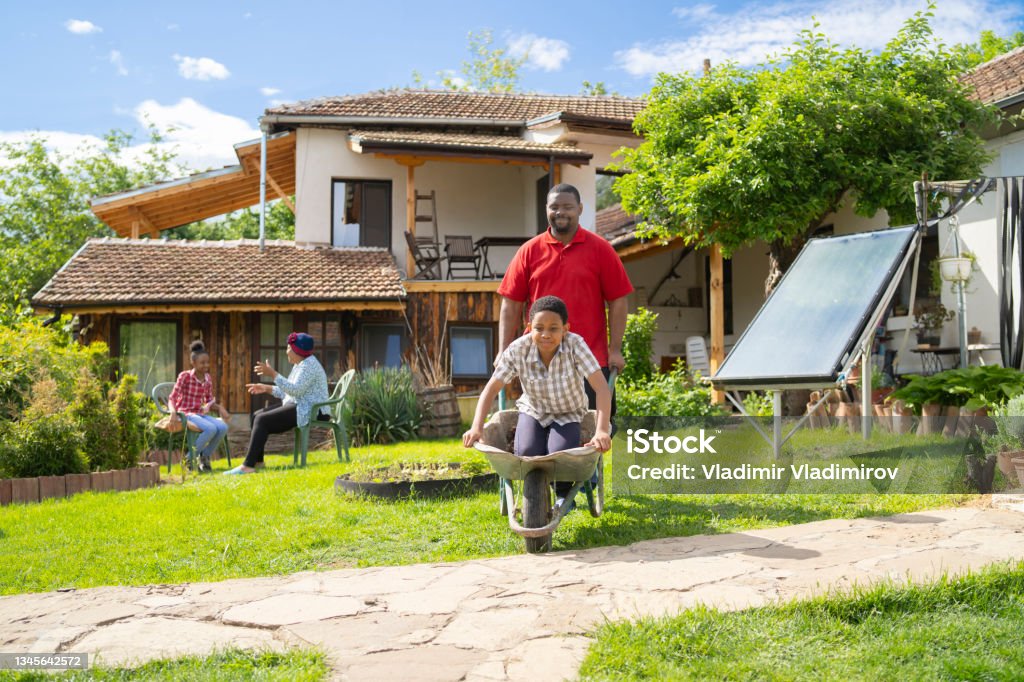 Afro-American dad is driving his son in a whellbarrow Happy boy and his dad having fun outdoors. Dad is driving him in a wheelbarrow. Solar Panel Stock Photo