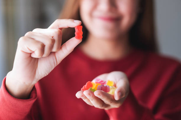 a young woman holding and showing at a red jelly gummy bears Closeup image of a young woman holding and showing at a red jelly gummy bears gummy candy photos stock pictures, royalty-free photos & images