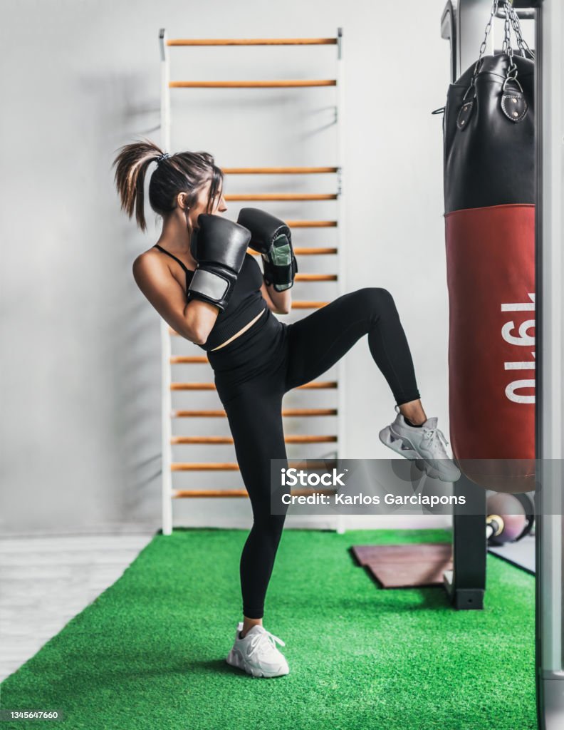ein vollmundiges Mädchen mit schwarzen Boxhandschuhen tritt gegen eine Trainingstasche. - Lizenzfrei Kickboxen Stock-Foto ein vollmundiges Mädchen mit schwarzen Boxhandschuhen tritt gegen eine Trainingstasche. - Lizenzfrei Kickboxen Stock-Foto