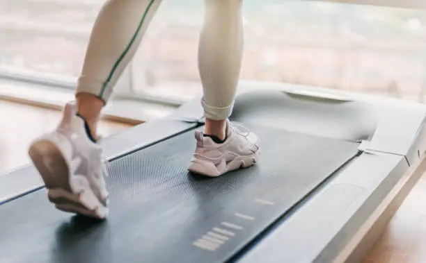 selectively blurred detail of legs running on a treadmill. a warm light enters through the window in the background.