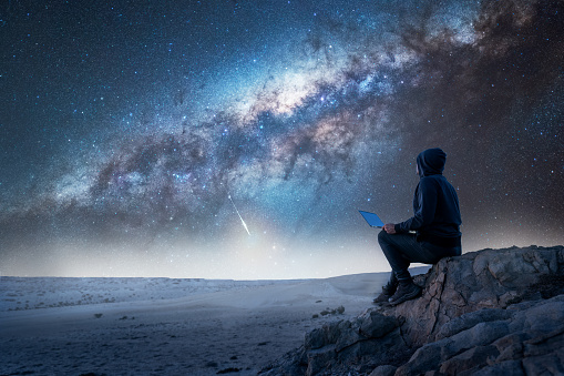 silhouette of a person sitting on the top of the mountain with laptop staring the Milky Way at night