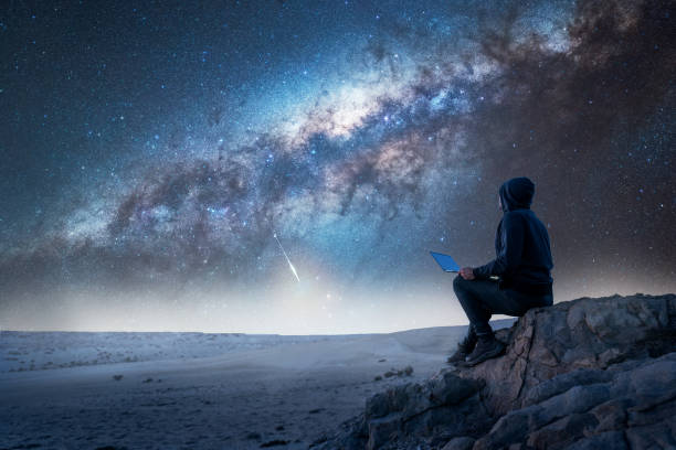 sylwetka osoby siedzącej na szczycie góry z laptopem wpatrującej się nocą w drogę mleczną - milky way galaxy star astronomy zdjęcia i obrazy z banku zdjęć