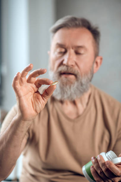 istock A bearded man holding a pill and looking at it 1345648827