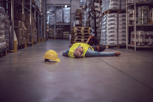 Senior Warehouse Worker Lying Unconscious on the Concrete Floor After the Fall. Injury at Work.