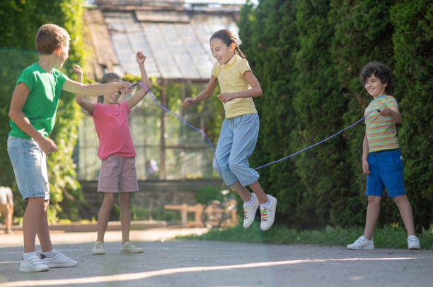 Girl with pigtails jumping rope with friends Happy childhood. Cheerful laughing school-age girl with pigtails jumping rope with friends spending free time in park on sunny day jump rope stock pictures, royalty-free photos & images