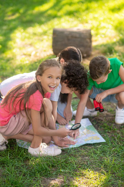 istock Enthusiastic girl with magnifying glass and friends with map 1345656363