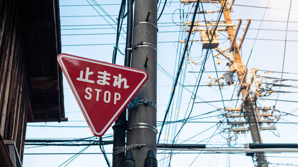 Red triangular stop warning traffic road sign with white letters kanji standing at the local street junction in Japan. Translation of the word in Japanese means stop