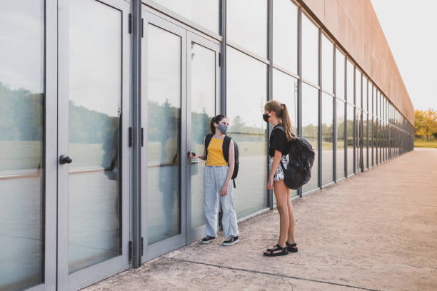 istock Teenage students with protective mask and backpack speaking at modern school. 1345656803