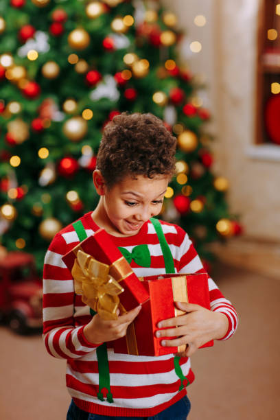istock A black boy holds and open a box with a Christmas gift, on the Christmas tree background 1345657589