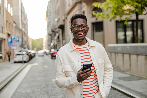 The portrait of an African-American man is on the street, he is walking and using a mobile phone on the go