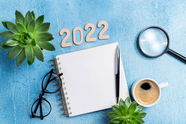 istock New year resolutions 2022 on desk. 2022 goals with notebook, coffee cup and eyeglasses on blue background. Goal, plan, strategy, action, idea concept 1345666244