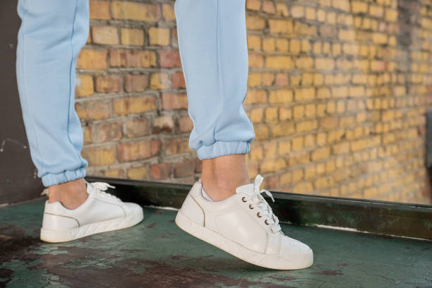 Unrecognizable woman in leather shoes with shoelaces. Women's sports pants. Casual comfortable clothing for everyday.Woman's legs in blue pants and white shoes. Unrecognizable young runner tying her shoelaces. Studio shot on wooden floor background. jogging pants stock pictures, royalty-free photos & images