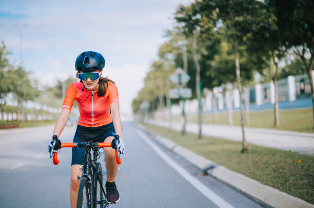 asiatische chinesische junge radfahrerin, die am wochenendmorgen in der stadtstraße rennrad fährt - cyclist cycling road women stock-fotos und bilder