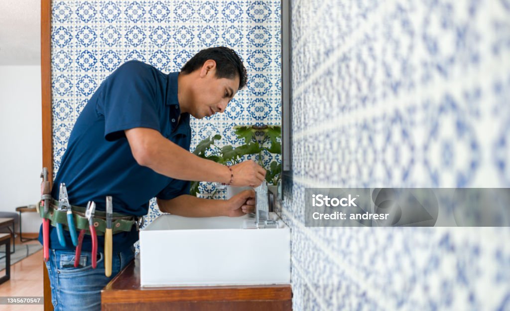 Plumber installing a faucet in a bathroom's sink Latin American Plumber fixing a leak in a faucet in a bathroom's sink - home repairment concepts Plumber Stock Photo