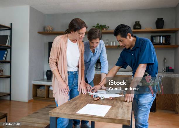 Plumber Fixing A Pipe And Talking To His Clients In The Kitchen Stock Photo - Download Image Now