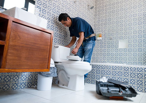 Fontanero latinoamericano arreglando un inodoro en el baño photo