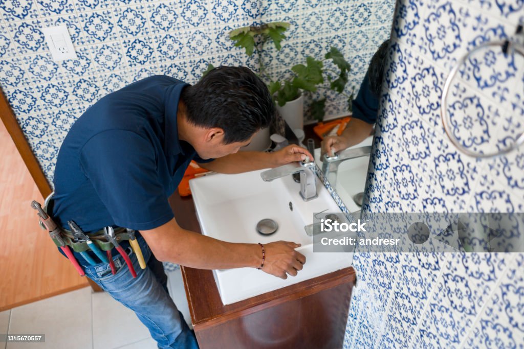 Plumber installing a faucet in a bathroom's sink Latin American plumber installing a faucet in a bathroom's sink - home repairment concepts Bathroom Stock Photo