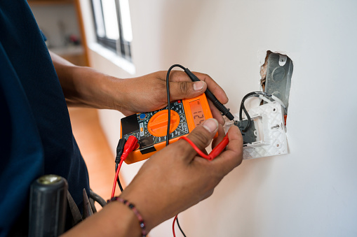 Close-up on an electrician fixing an electrical outlet and measuring the voltage at a house - home improvement concepts