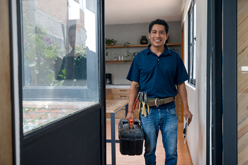 Latin American Happy plumber or electrician arriving home after a house call and holding his toolbox - blue-collar worker concepts