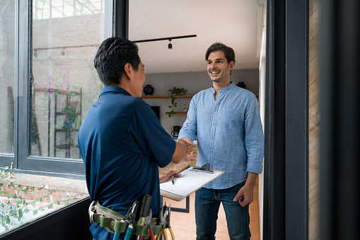 Latin American Electrician or plumber greeting a client with a handshake at the door of his house
