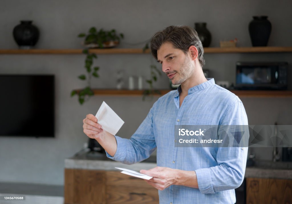 Happy man at home checking letters in the mail Portrait of a happy Latin American man at home checking letters in the mail and smiling - domestic life concepts Mail Stock Photo
