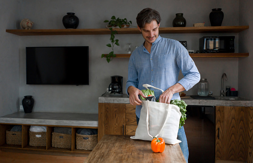 Happy Latin American man arriving home with the groceries using reusable bags