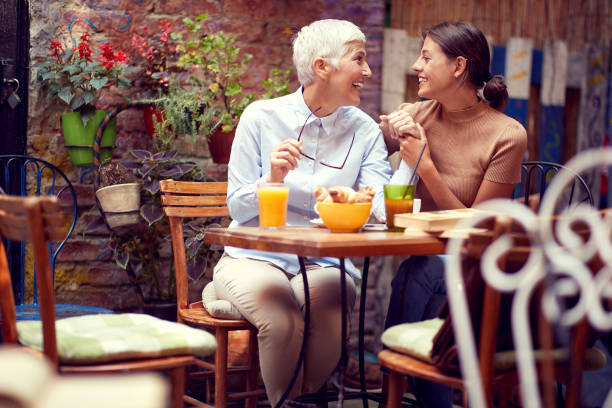 due donne caucasiche, anziane e giovani, che parlano, si guardano, sorridono. - women juice drinking breakfast foto e immagini stock