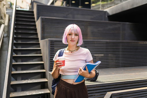 Imagen de una mujer joven con cabello colorido en el campus universitario y sosteniendo una taza de café sostenible photo