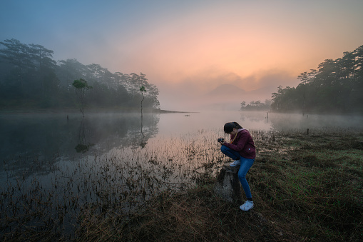 Vietnamese girl is taking photos by the Tuyen Lam lake in a foggy morning- Da Lat, Lam Dong province, central highlands Vietnam