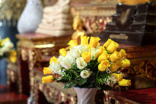 Close-up at colorful artificial flower bush which is placed on set of altar table in front of golden Buddha statue in the temple. Religion interior decoration object photo. Selective focus.