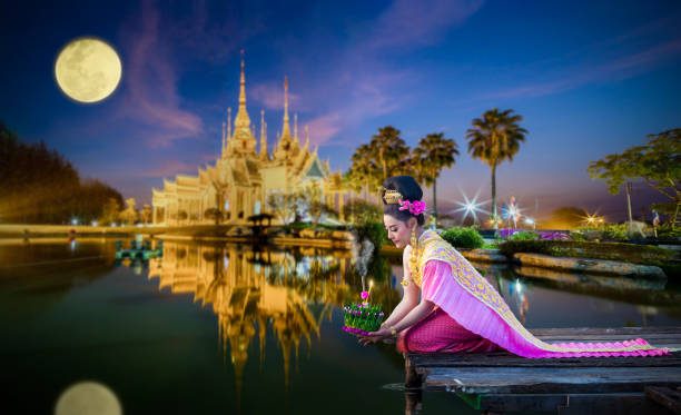 Beautiful Thai woman in Loy Krathong Festival of Thailand. Beautiful Thai woman in Thai traditional costume on the wooden floor and holding floating basket (Krathong in Thai language) for floating in the red lotus lake in Loy Krathong Festival of Thailand. loi krathong stock pictures, royalty-free photos & images