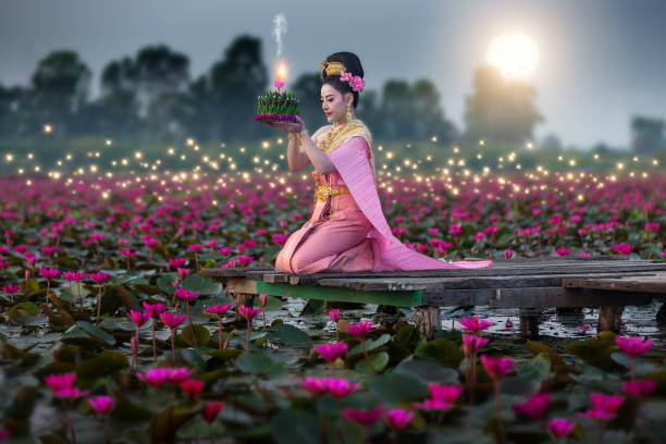 Beautiful Thai woman in Loy Krathong Festival of Thailand. Beautiful Thai woman in Thai traditional costume on the wooden floor and holding floating basket (Krathong in Thai language) for floating in the red lotus lake in Loy Krathong Festival of Thailand. loi krathong stock pictures, royalty-free photos & images