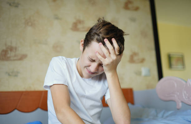 Teen with headache Child sitting on bed with headache. Negative emotions headache stock pictures, royalty-free photos & images