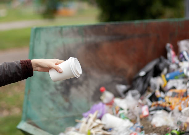 istock Woman throwing a cardboard glass into a recycling bin. large trash bin 1345684945