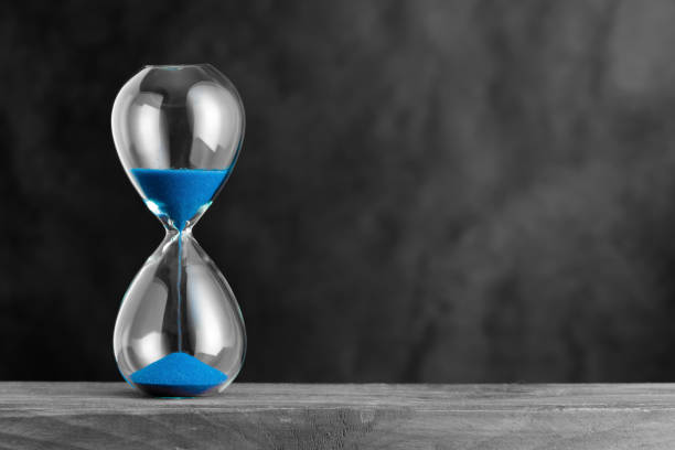 istock Hourglass with blue sand on the wood 1345685951