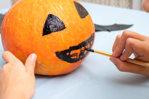 istock Hand drawing a scary face on an orange pumpkin with a brush to create a Halloween Jack Lantern, close-up 1345687401
